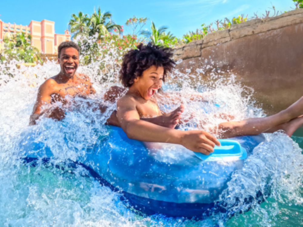 Two kids on a dual-person water float going down a water slide